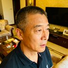 一位中年男性球迷王志强的头像，短发，穿着深色polo衫，表情专注，背景为家庭客厅环境